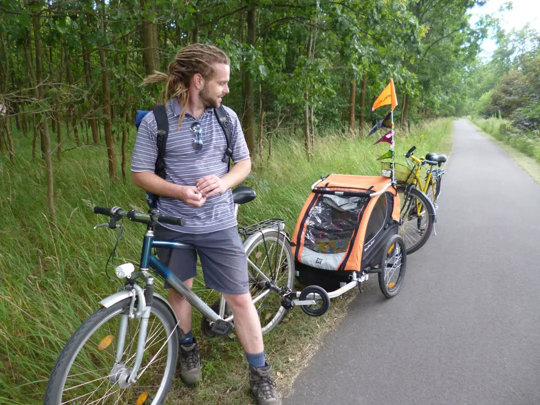 Adam with a child bike trailer, on a tree-lined path in Berlin.