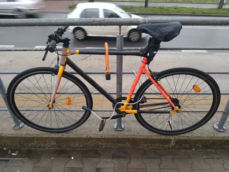 Bicicleta asegurada con candado U y cable: cuadro y ruedas atadas a un poste fijo.