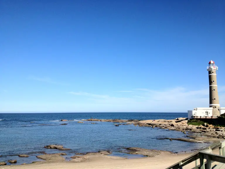 A calm bay and rocks; on the right, a stone lighthouse banded in white with a red lantern.