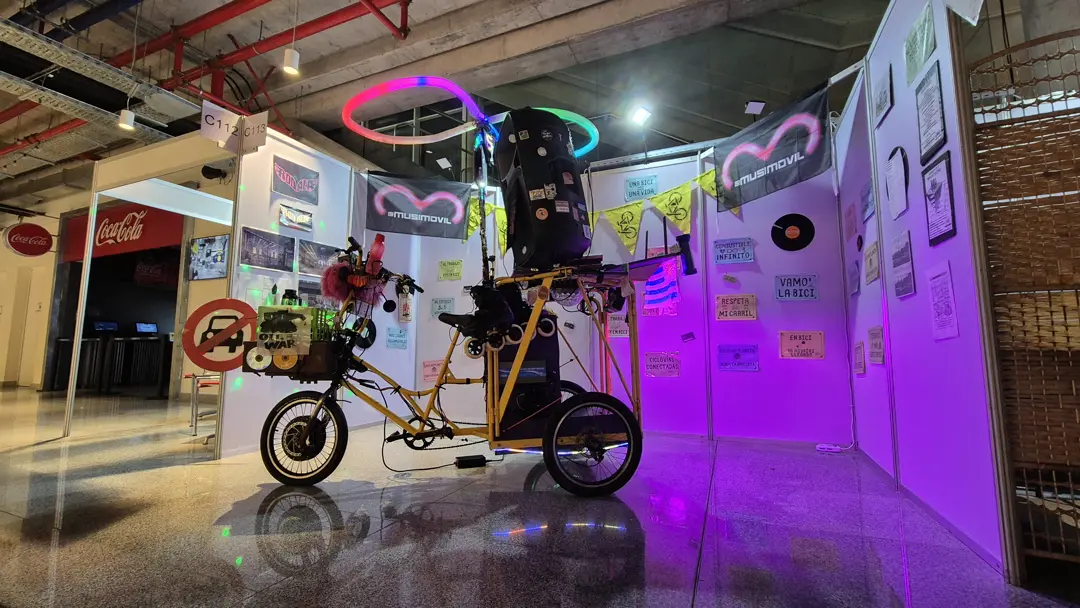 The MusiMóvil on show at an expo stand, surrounded by hand-painted signs carrying pro-cycling slogans and two of the collective's flags.