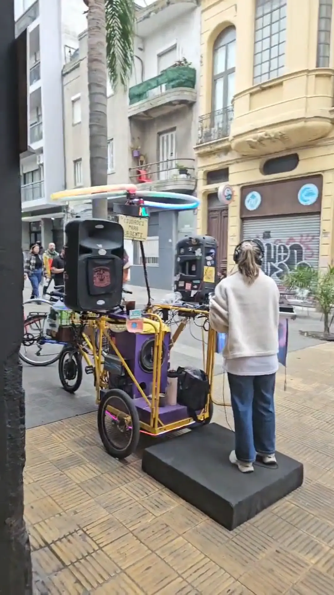 El MusiMóvil estacionado en la puerta de Rodala, sobre la peatonal Sarandí: triciclo violeta y amarillo con parlante, aro de neón en forma de infinito y un DJ sobre la plataforma trasera.