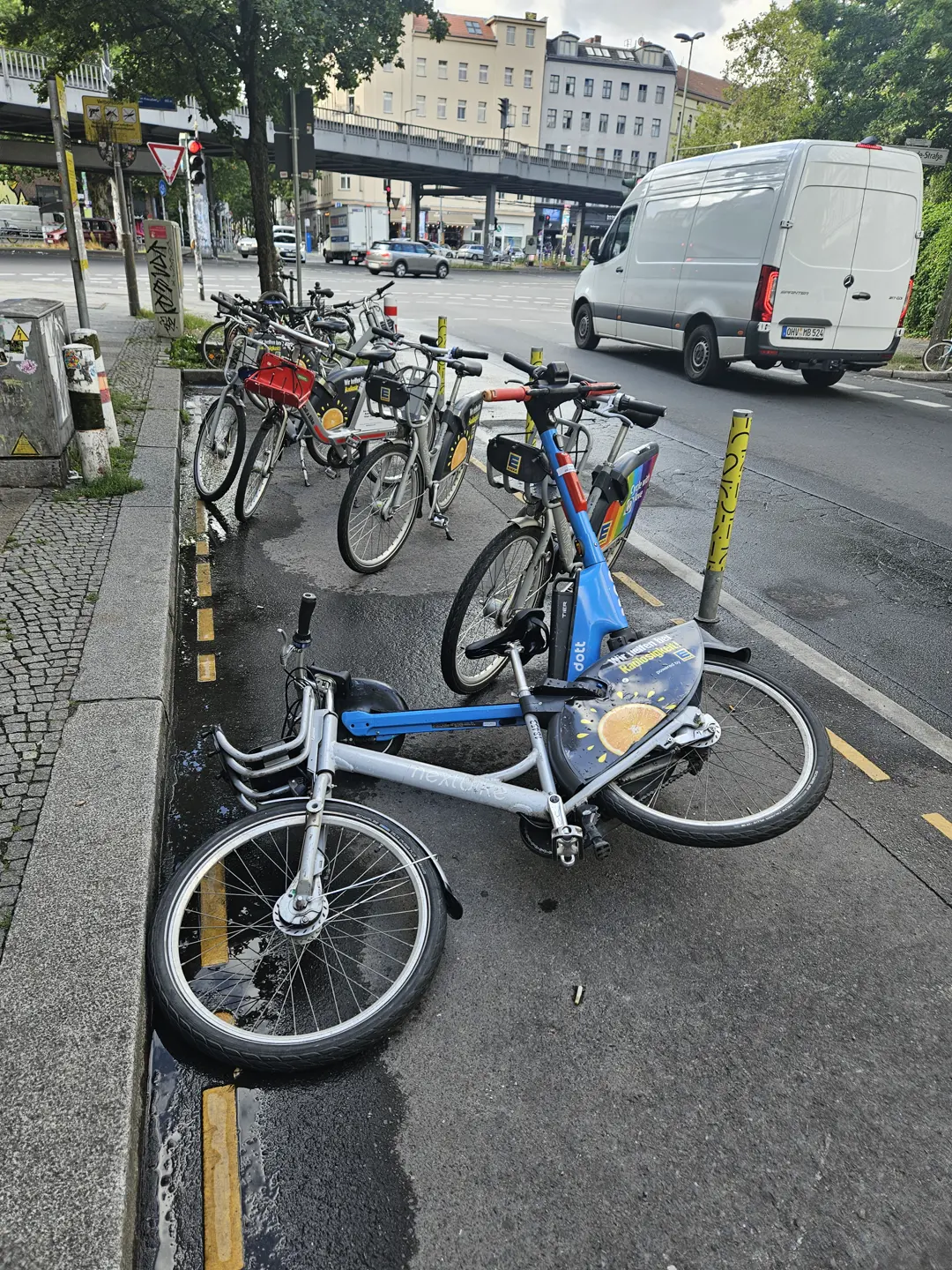 A shared bike down at the kerb's edge, among others left standing.